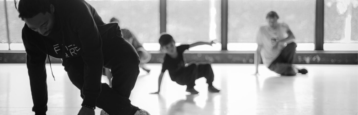 Photo en noir et blanc. Danseur en premier plan donnant des cours à des personnes en second plan.