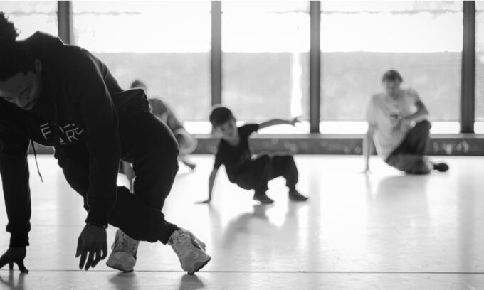 Photo en noir et blanc. Danseur en premier plan donnant des cours à des personnes en second plan.