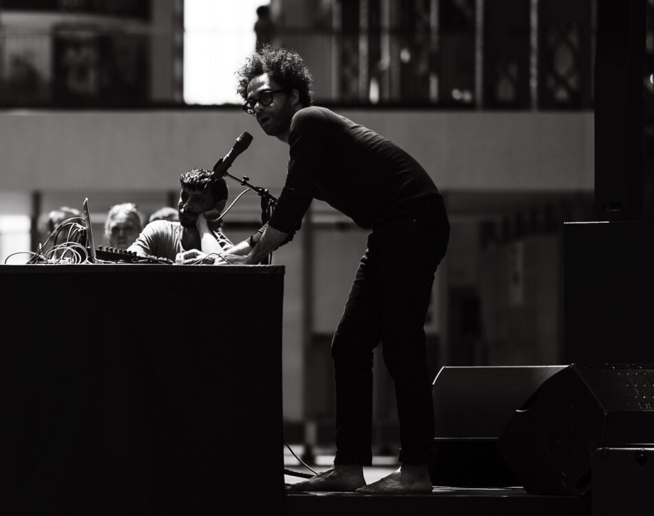 Photo en noir et blanc. Homme parlant à un micro durant le spectacle Crack.