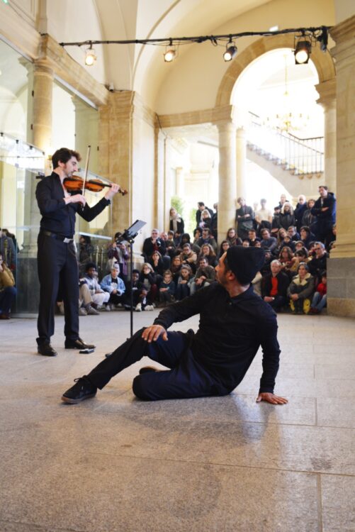 Danseur en mouvement regardant le violoniste avec spectateur en fond.