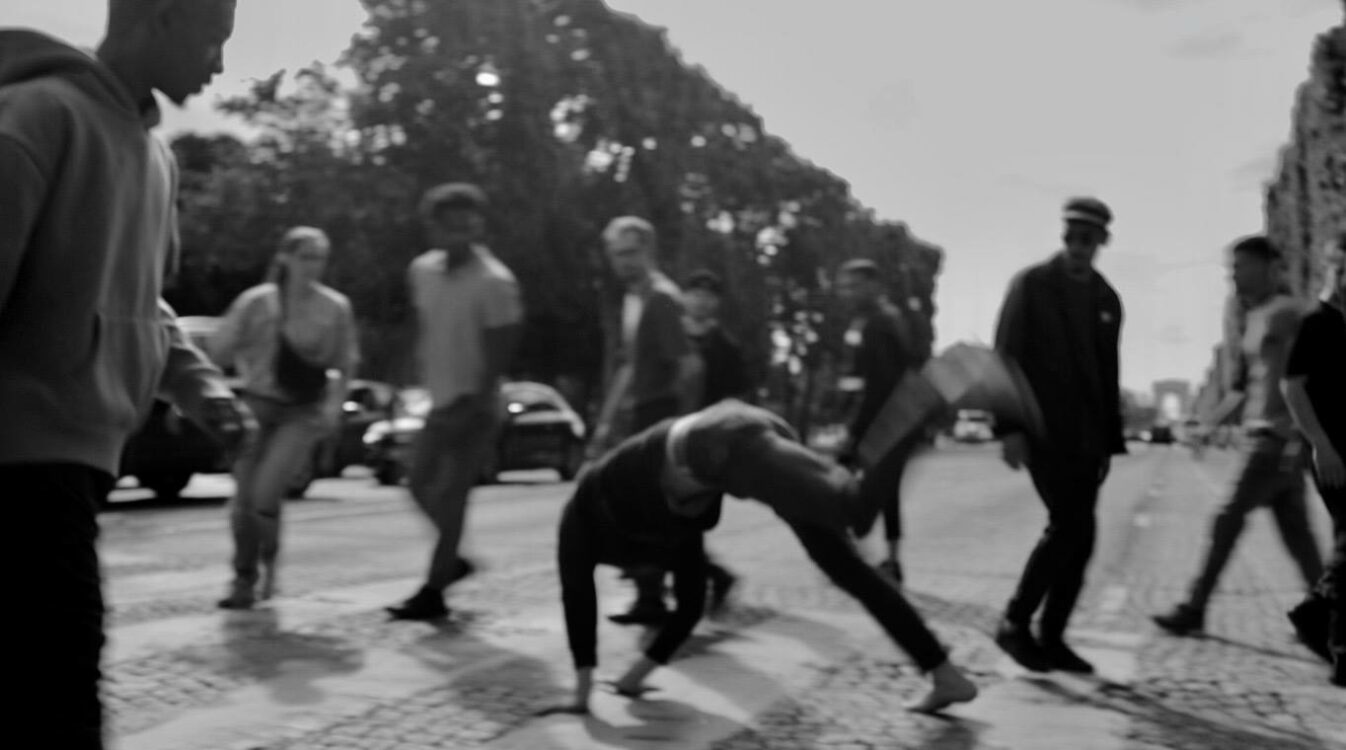 Photo en noir et blanc d'un danseur en mouvement sur un passage piéton, des personnes le regardent.