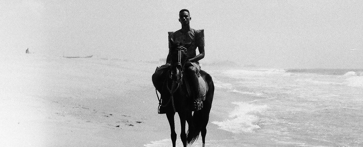 Photo en noir et blanc. Personne à cheval au bord de plage.