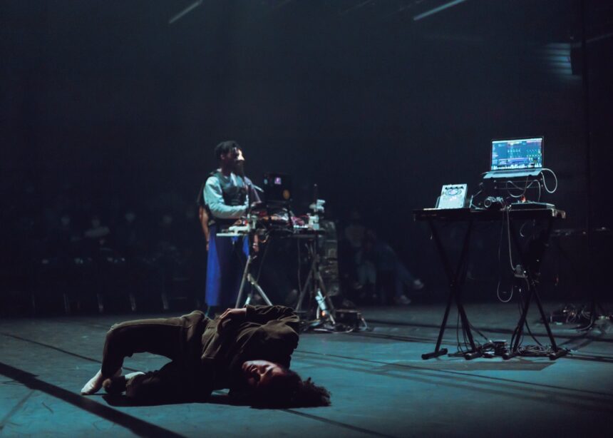 Danseur en mouvement au premier plan avec un musicien et le public en fond durant le spectacle Earthbound.