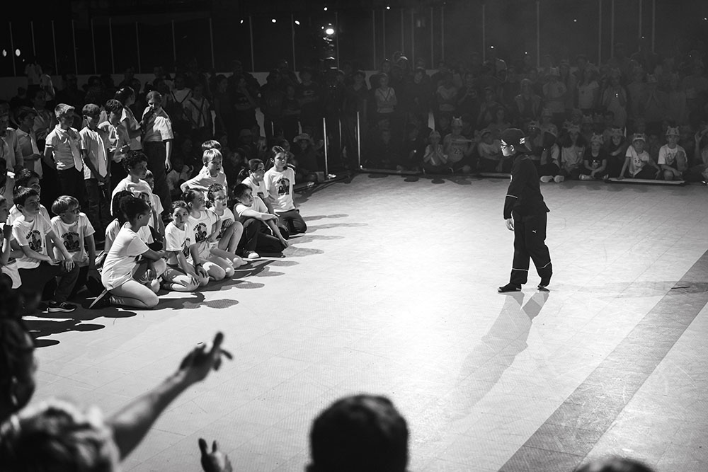 Photo en noir et blanc. Un enfant sur le devant face à d'autres qui danse durant une des battle.
