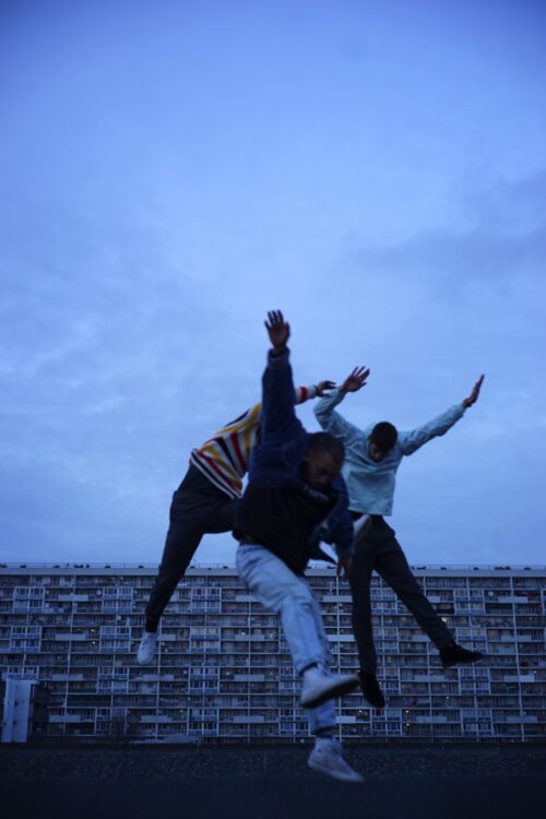 Trois danseurs en mouvement. Fond est un immeuble en large.