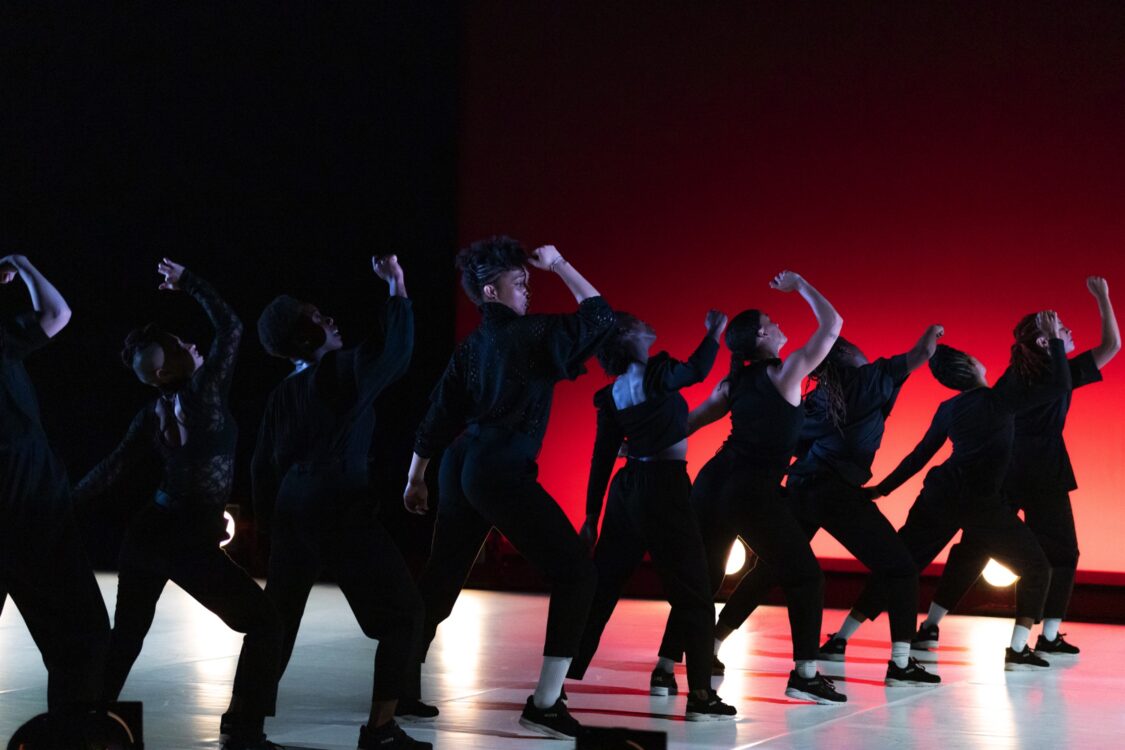 Danseuses sur scène, en mouvement. Le fond est rouge et elles sont en noir.