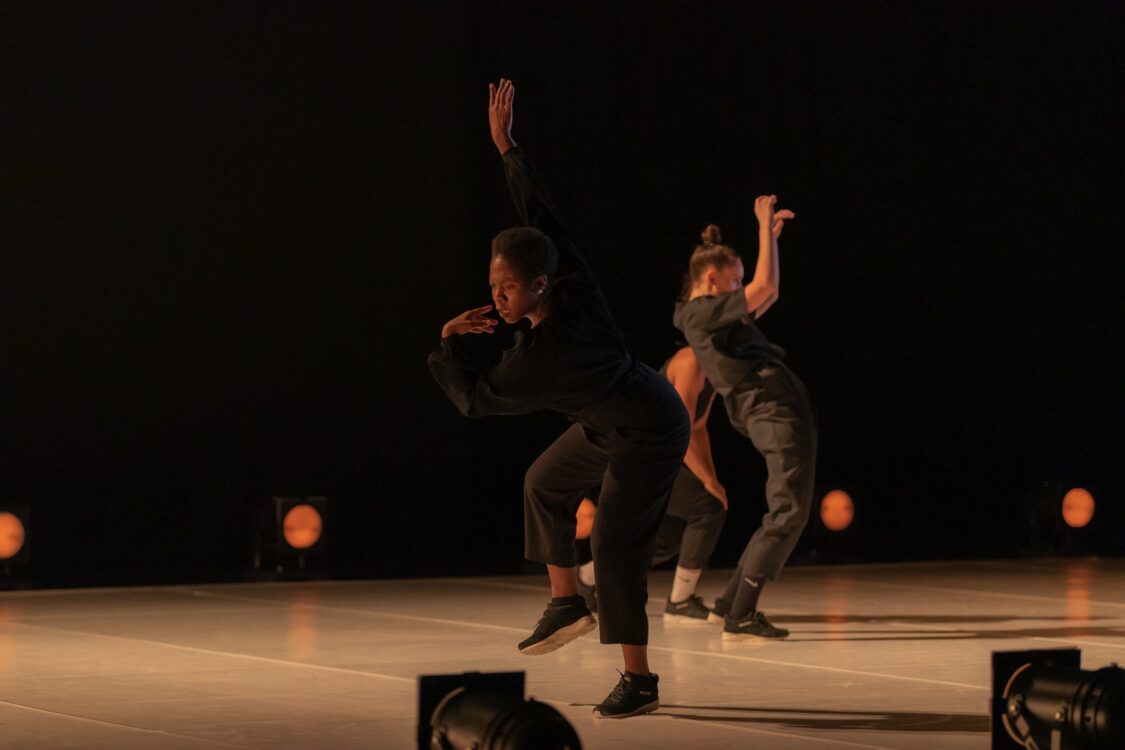 Danseuse en mouvement sur le devant de la scène. En fond, deux danseuses en mouvement.