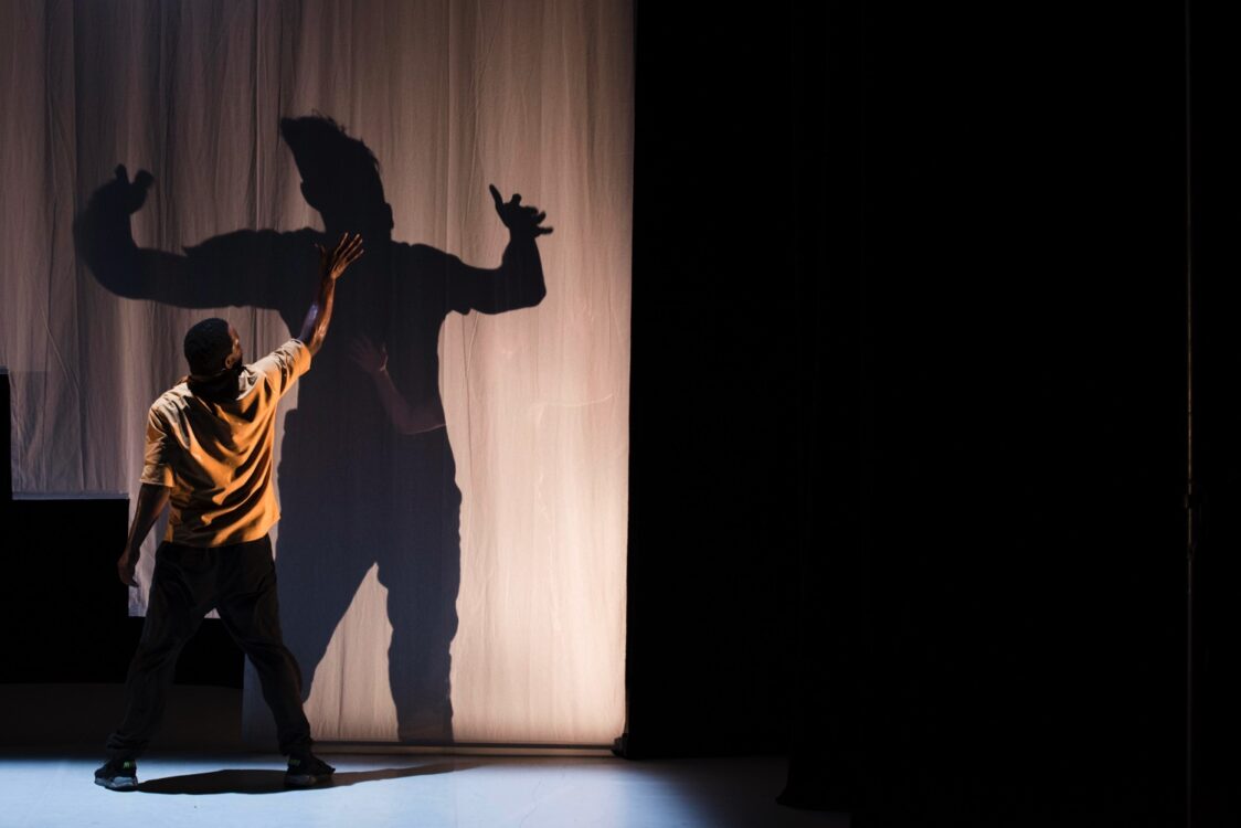 Danseur face à un drap, bras levé. Un autre danseur de l'autre côté.