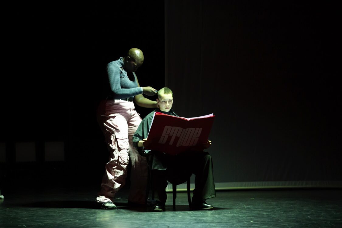Danseuse rasant une autre assise sur une chaise et lisant un grand magazine Stuck.